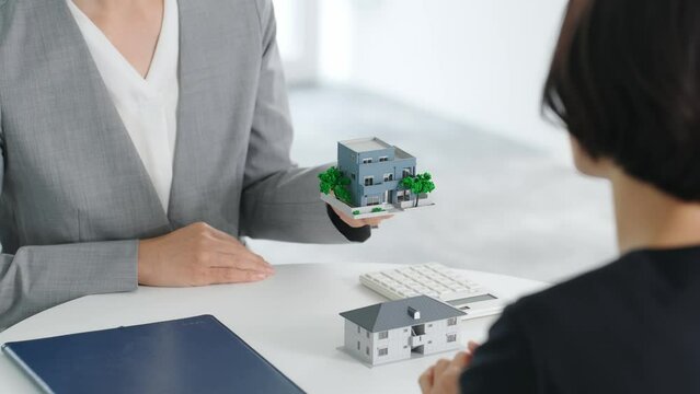 オフィスで住宅模型を持って会話する二人の女性ビジネスパーソン