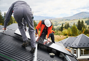 Installers building photovoltaic solar module station on roof of house. Men electricians in helmets...