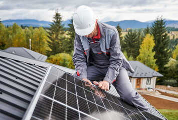Professional engineer securing solar cell on roof by hexagon tool. Solar PV panel installation. Male worker installating solar battery on a roof on background of forest