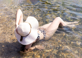 a girl in a swimsuit and a hat lies in the sea water near the shore