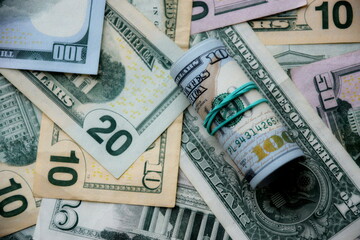 Hundred dollar bills roll lies on big amount of US dollars in different nominations under natural light