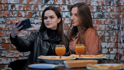 Two beautiful stylish young girls have lunch in a cafe and take a selfie