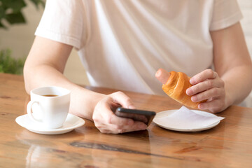 Woman in a white T-shirt with a cup of coffee and a sausage at a table in a café