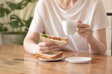 Woman in a white T-shirt with a cup of coffee and a sandwich at a table in a café