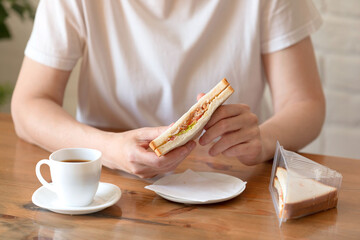 Woman in a white T-shirt with a cup of coffee and a sandwich at a table in a café