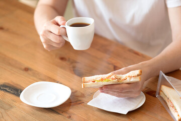 Woman in a white T-shirt with a cup of coffee and a sandwich at a table in a café
