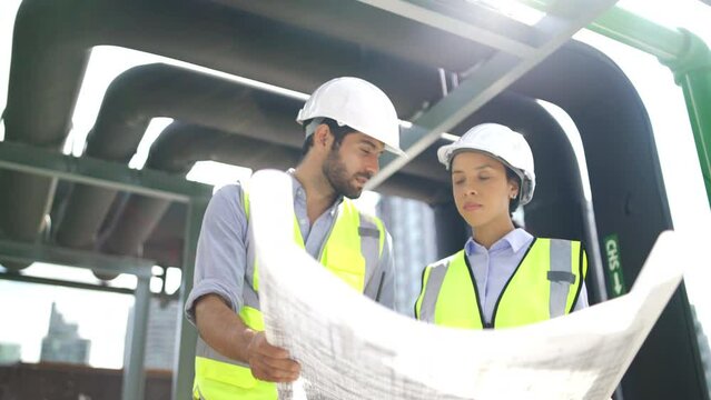Couple professional engineer discuss with blue print or plan paper of construction site and stay under the floating pipe or pipe hanging on deck of building.	