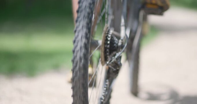 Abstract mountainbiker getting ready to ride. Man riding a mountainbike on a dusty dirth road path. Closeup pedal shoe and gear shift. Recorded at 120 fps on cinema camera.