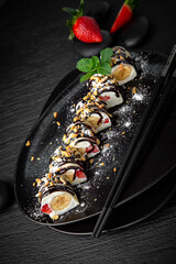 Japanese dessert sweet roll with banana, cream in rice paper. Composition on black background. The Art of Japanese Cuisine. Food photography for menu and sushi bar decoration