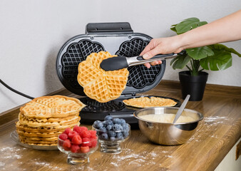 Making Belgian waffles. Female hand pours dough into waffle maker in kitchen at home. Cooking summer breakfast with round waffles and berries