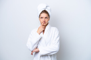 Teenager Russian girl in a bathrobe isolated on white background having doubts while looking up