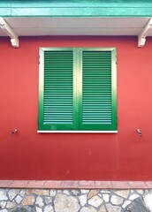 Fototapeta premium Green window with shutters on a red wall of an old house