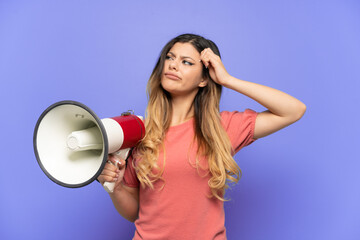 Young Russian girl isolated on blue background holding a megaphone and having doubts