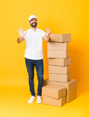 Full-length shot of delivery man among boxes over isolated yellow background counting eight with fingers