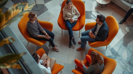 A diverse group of people engage in a lively discussion in a stylish, contemporary setting seen from above. AIG53M
