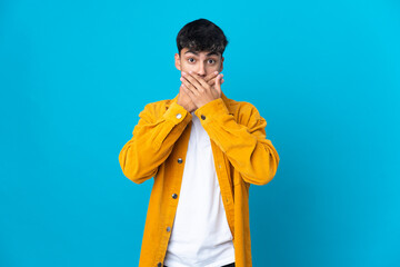 Young man over isolated blue background covering mouth with hands