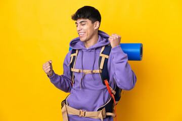 Young mountaineer man with a big backpack over isolated yellow background celebrating a victory