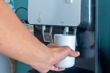 A male hand filling a cup with water from water cooler or water dispenser