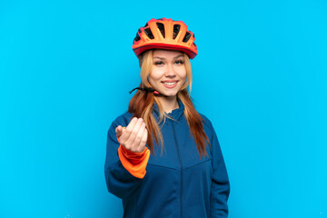 Young cyclist girl isolated on blue background inviting to come with hand. Happy that you came