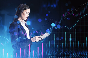 A professional woman reviews data on a tablet with digital stock market graphs overlaying the blue background, depicting financial analysis