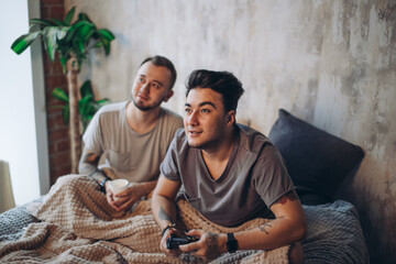 Adult relationships. Two same-sex male partners resting together in one bed, having morning coffee. Romantic love. Homosexual couple