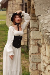 Brunette woman in vintage dress and hat standing at old brick wall