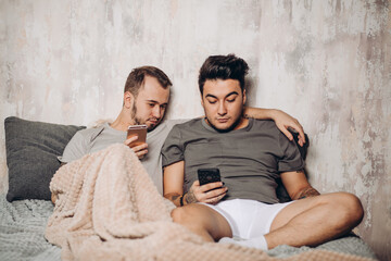 Perfect morning with beloved friend in bed. Two happy handsome guys resting in bed and watching...