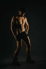 A fit male showcasing his defined abs and muscular arms in a low-light setting, emphasizing strength and fitness.