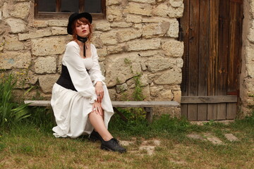 Old fashioned young woman sitting on a bench at ancient stone house