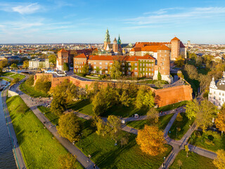 Krakow, Poland. Royal Wawel castle and cathedral, Vistula river, boulevards, promenades and autumn trees with golden leaves. Walking people and bikers. Aerial view in sunset light
