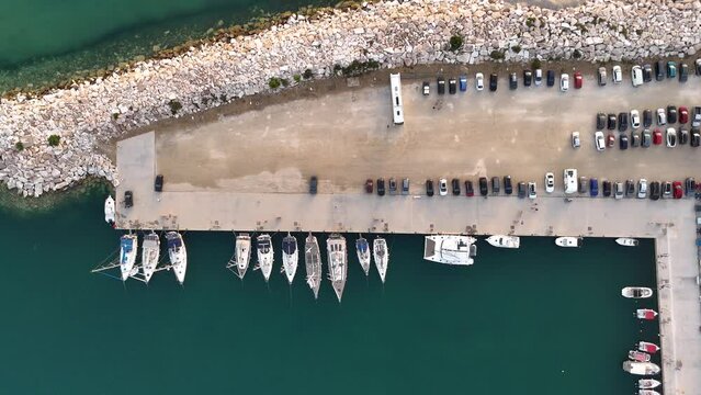 Luxury yachts and sailboats docked at the marina with parked cars in Limenaria, Thasos island, Greece. Aerial drone top down view