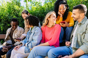 Group of multiracial young people using mobile phone devices sitting outdoors. Millennial happy students addicted to social media app