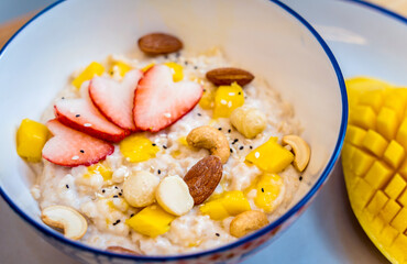 A bowl of oats with strawberries and mango arranged on a plate