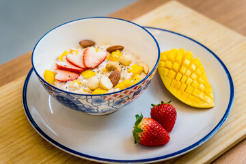 A bowl of oats with strawberries and mango arranged on a plate