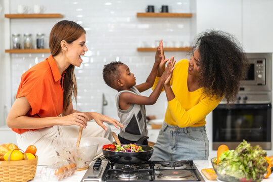 Diversity young happy love LGBT, LGBTQ caucasian and african family lesbian couple woman cook vegan food healthy eat with fresh vegetable salad in kitchen at home, pride, rainbow.Lgbt lesbian couple