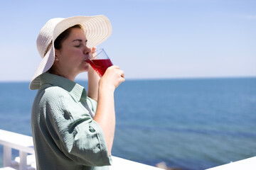 a young woman in a straw hat drinks a cocktail against the background of the sea