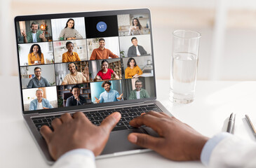 A persons hands are visible typing on a laptop while a virtual meeting with several participants is...