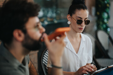 Two business partners discussing their new project and analyzing statistics together in a modern coffee shop setting.