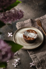 Fresh homemade chocolate muffin close up on a rustic plate with lilac flowers
