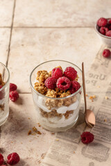 Berry dessert in glass with granola, fresh raspberries, yogurt or cream cheese. Healthy breakfasr concept, on beige tile background with text space