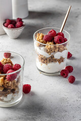 Berry dessert in glass with granola, fresh raspberries, yogurt or cream cheese. Healthy breakfasr concept, vegetarian on gray background