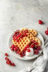 Homemade waffles with summer berries and a scoop of ice cream in plate on grey table with text space. Heart shaped waffles