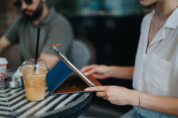 Casual business meeting in a coffee shop. Close-up of female hands using tablet and iced coffee on table.