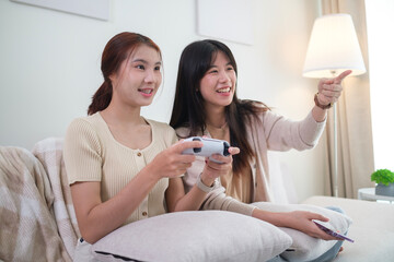 Happy Asian lesbian lgbt women couple having fun at home playing video games playing video game on couch.