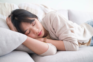 Serene young Asian woman sleeping on comfortable sofa  in living room, relaxation during weekend at home.