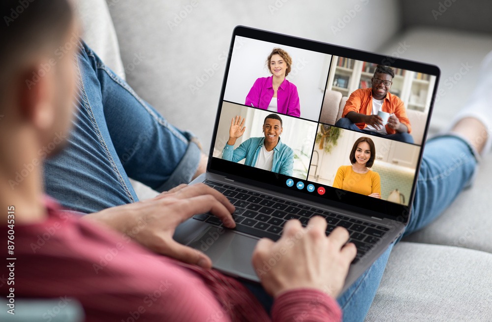 Poster a man sits on a couch with his legs extended and uses a laptop computer to participate in a video co