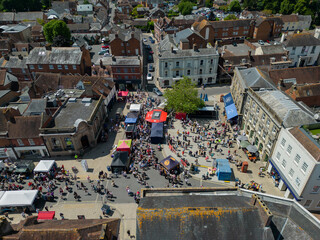 Wimborne Minster Folk Festival. Aerial view of the town square with people gathering ahead of street performance on a sunny weekend. Above old town with historic buildings. © Ssisabal