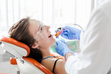 Dentist Taking Dental Impression of Smiling Patient. A dentist takes a dental impression of a smiling female patient wearing protective glasses. The patient is seated in an orange dental chair