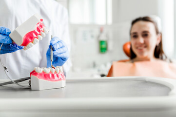 Dentist Demonstrating Dental Prosthetic Model. Dentist in blue gloves demonstrating a dental prosthetic model for patient education. The focus is on the dental model