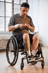 Obraz premium Vertical full length portrait of young basketball player with disability using finger tape preparing for match indoors